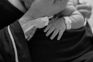 A black and white close-up photograph of two hands tenderly touching, showing a gentle emotional connection.