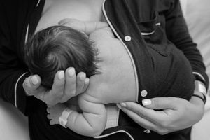 Black and white photo showing tender moment as parent cradles and holds tiny sleeping newborn baby against their chest.