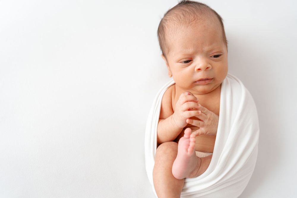 A peaceful sleeping newborn swaddled in a white wrap against a light background.