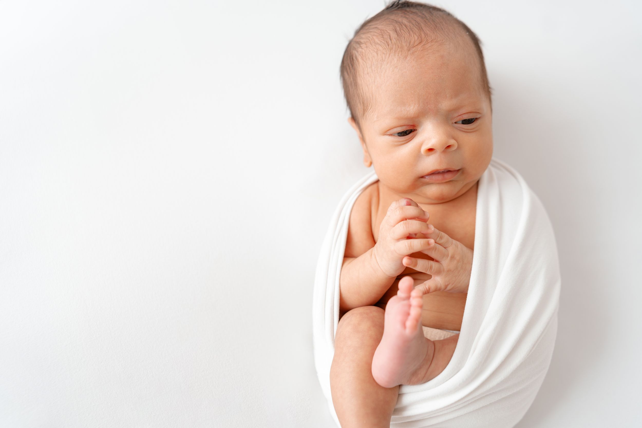 A peaceful sleeping newborn swaddled in a white wrap against a light background.
