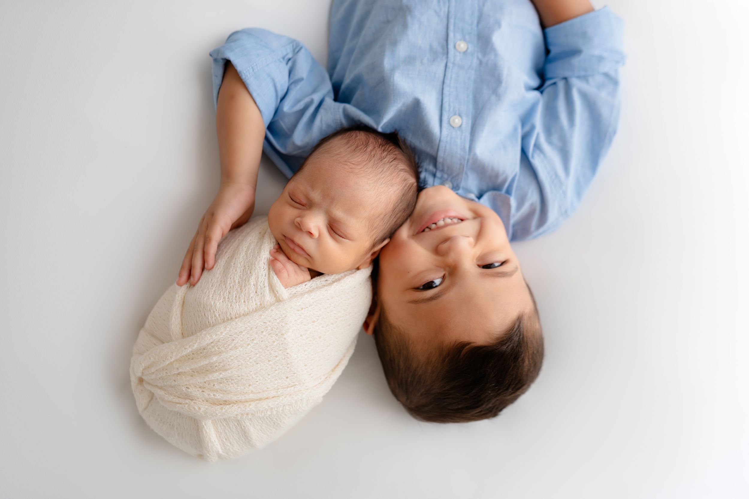 Two siblings in light blue and white appear side by side in portrait from above against a white background.