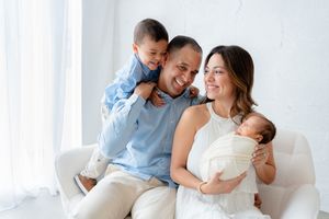 A happy family in white outfits sharing joyful moments together on a bright couch near a window.