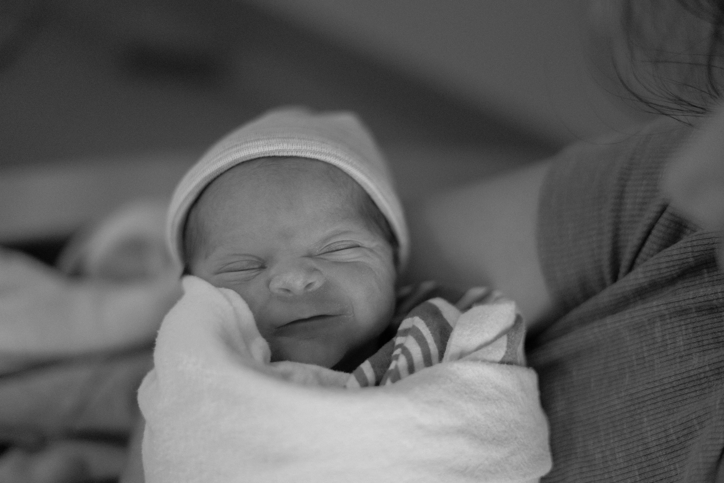 Black and white portrait of a newborn baby swaddled in soft blankets making a peaceful expression.