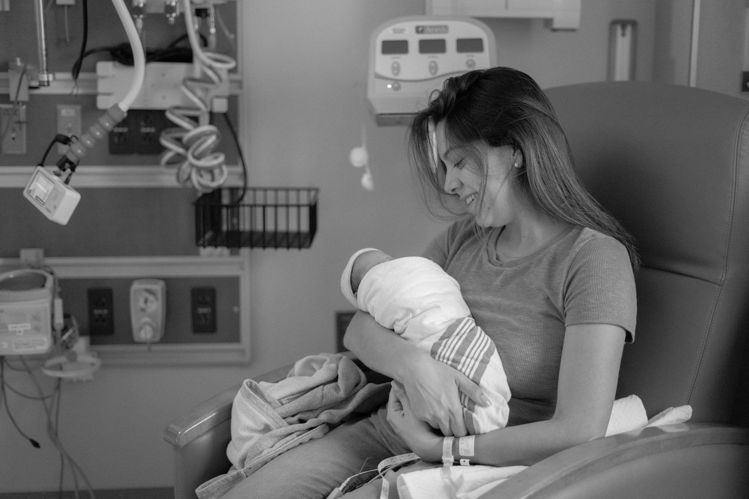 A tender moment in a hospital room as a parent cradles their newborn baby in black and white.