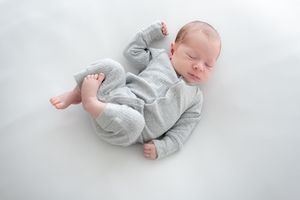 Peaceful sleeping newborn baby wearing soft gray onesie lying on white background.