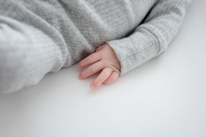 A small hand in a light gray sleeve rests on a white surface, creating a minimalist and peaceful composition.