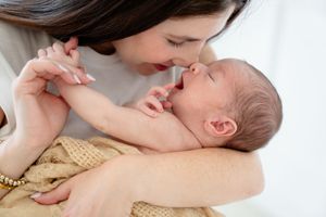 A tender moment shared between a parent and newborn baby lying on a beige blanket.