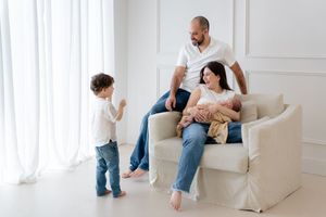 Family relaxing together in bright white living room on beige armchair near window.