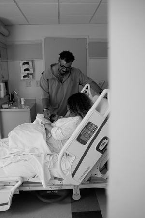 A doctor tends to a patient resting in a hospital bed in a black and white photograph.