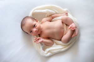 A newborn baby lies peacefully on a soft white blanket, curling their tiny toes and fingers.