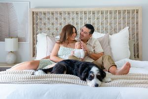 A couple relaxes on a white bed with their black and white dog while enjoying a cozy moment at home.