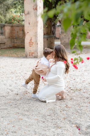 Parent and child share a tender moment in a garden setting with stone walls and pink flowers.
