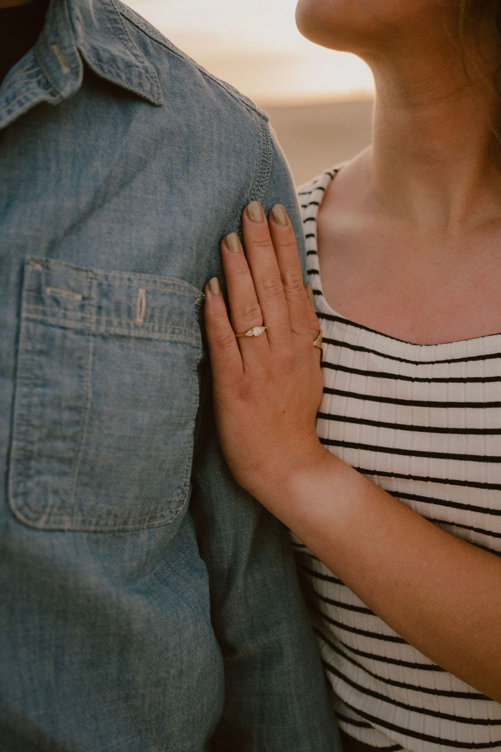 Close-up of engagement ring as woman's hand rests on denim shirt.