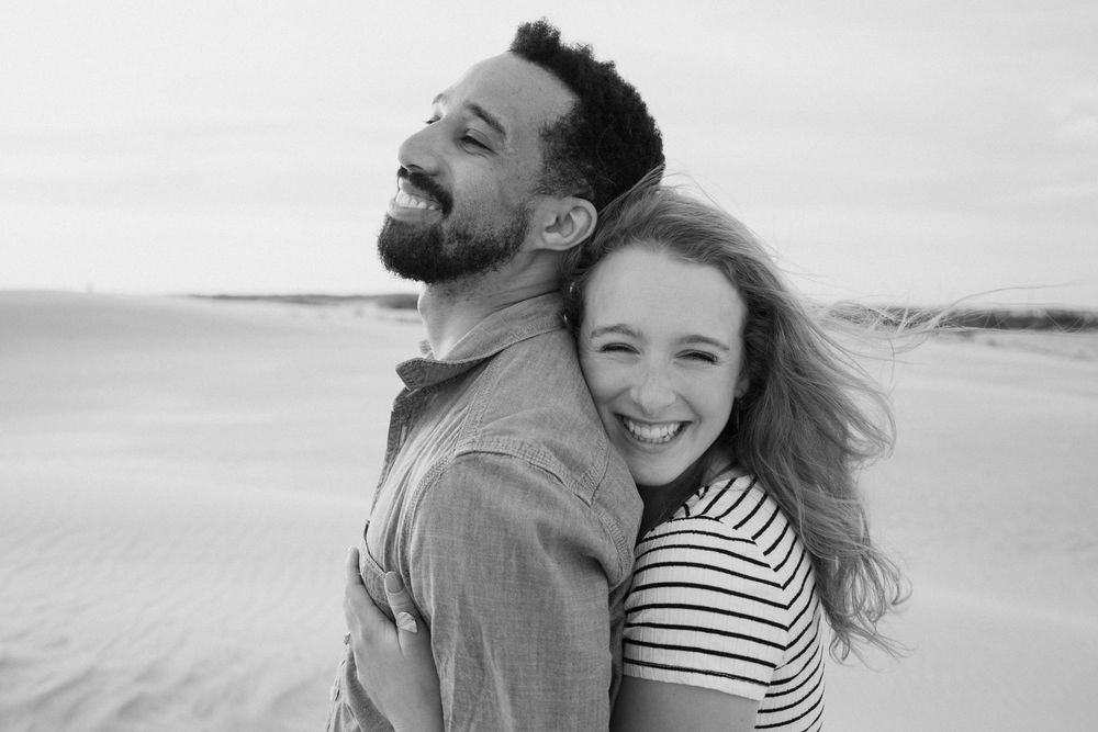 Black and white portrait of joyful couple embracing on beach.