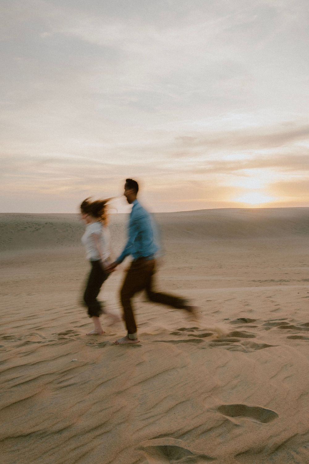Silhouetted couple dancing on sand dunes at sunset.