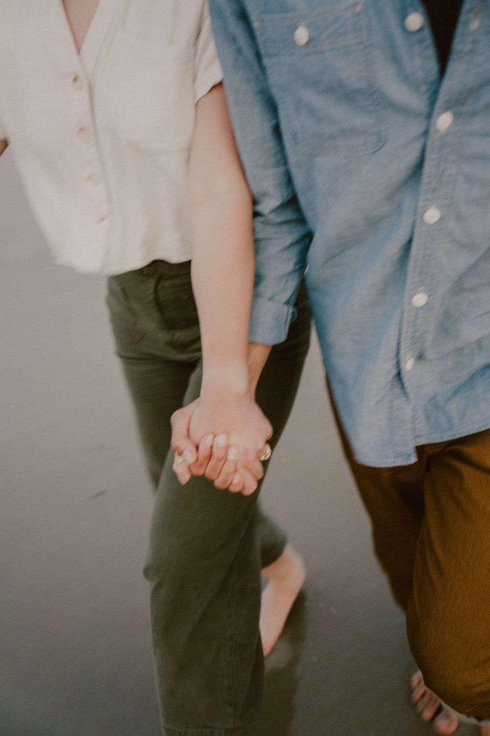 A couple in casual attire holding hands, wearing blue and white button-down shirts with olive and brown pants.