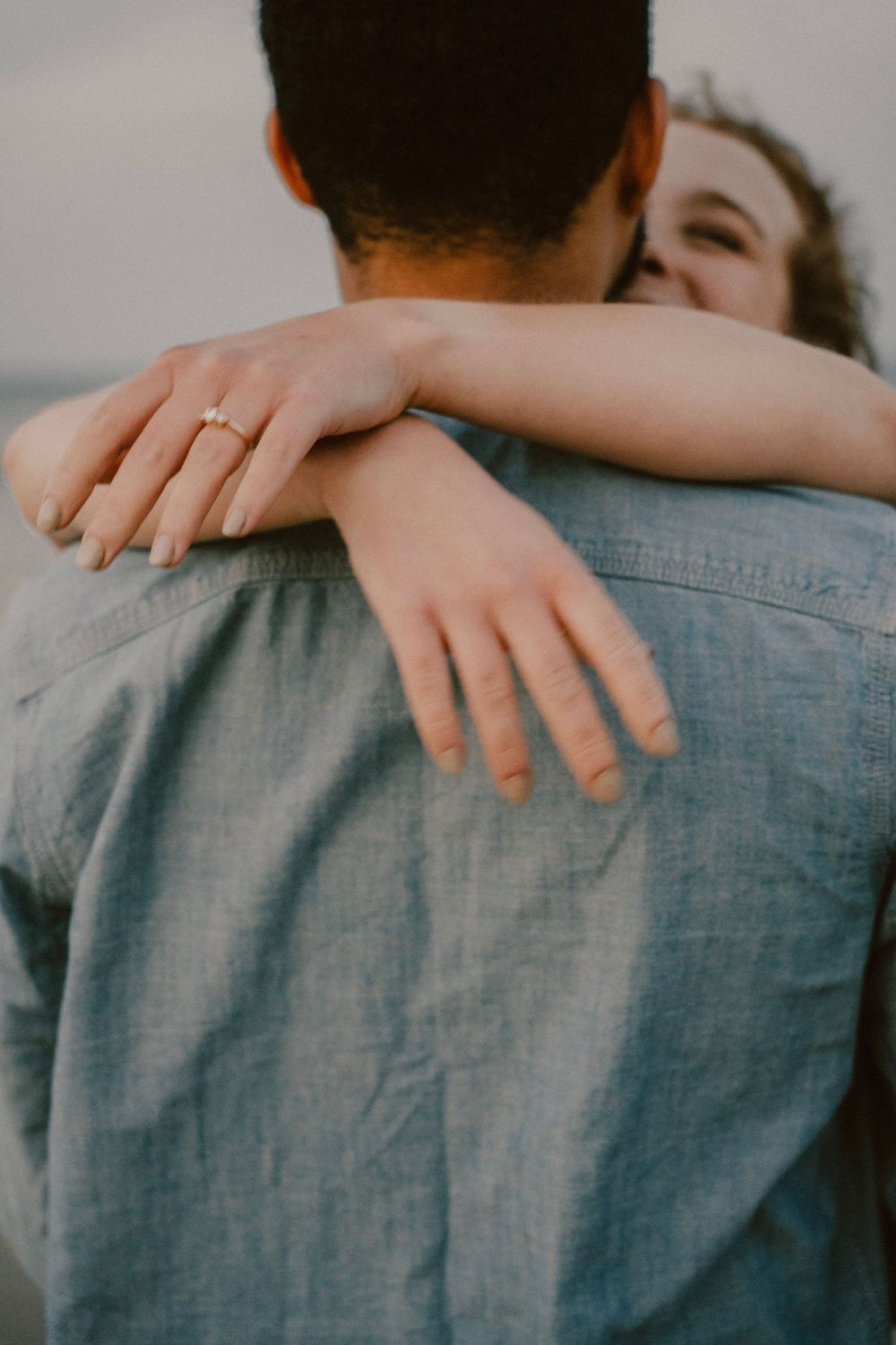 Close-up of a tender embrace showing arms wrapped around a denim-clad back.