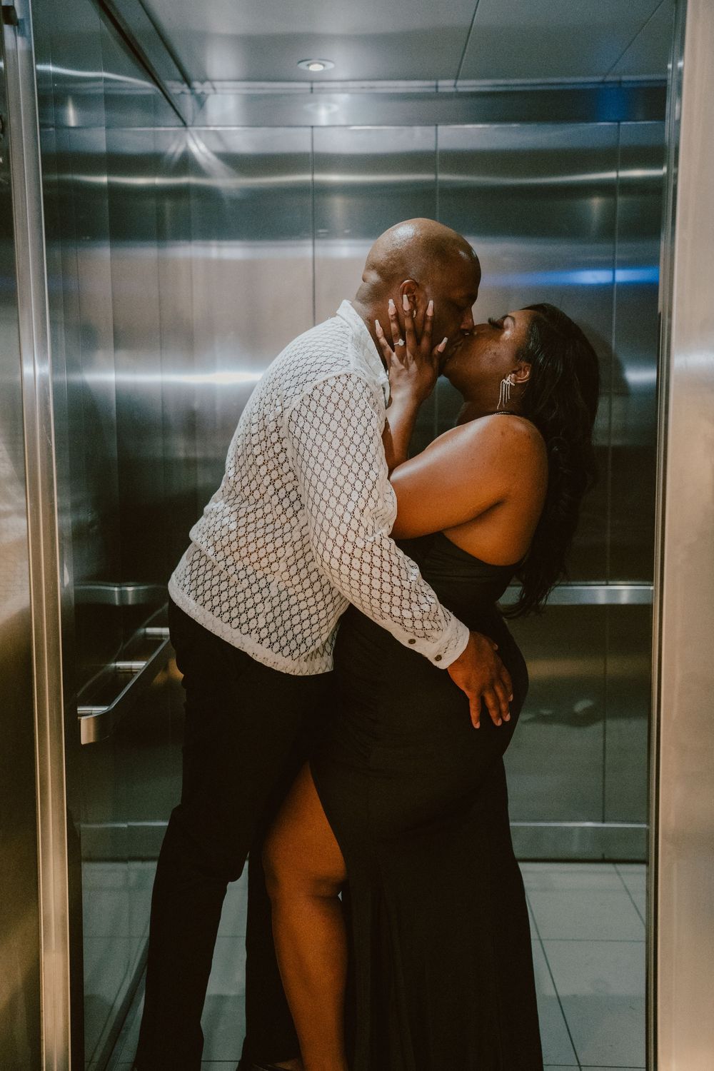 Intimate couple sharing a romantic moment in an elevator, with one wearing a white mesh top.