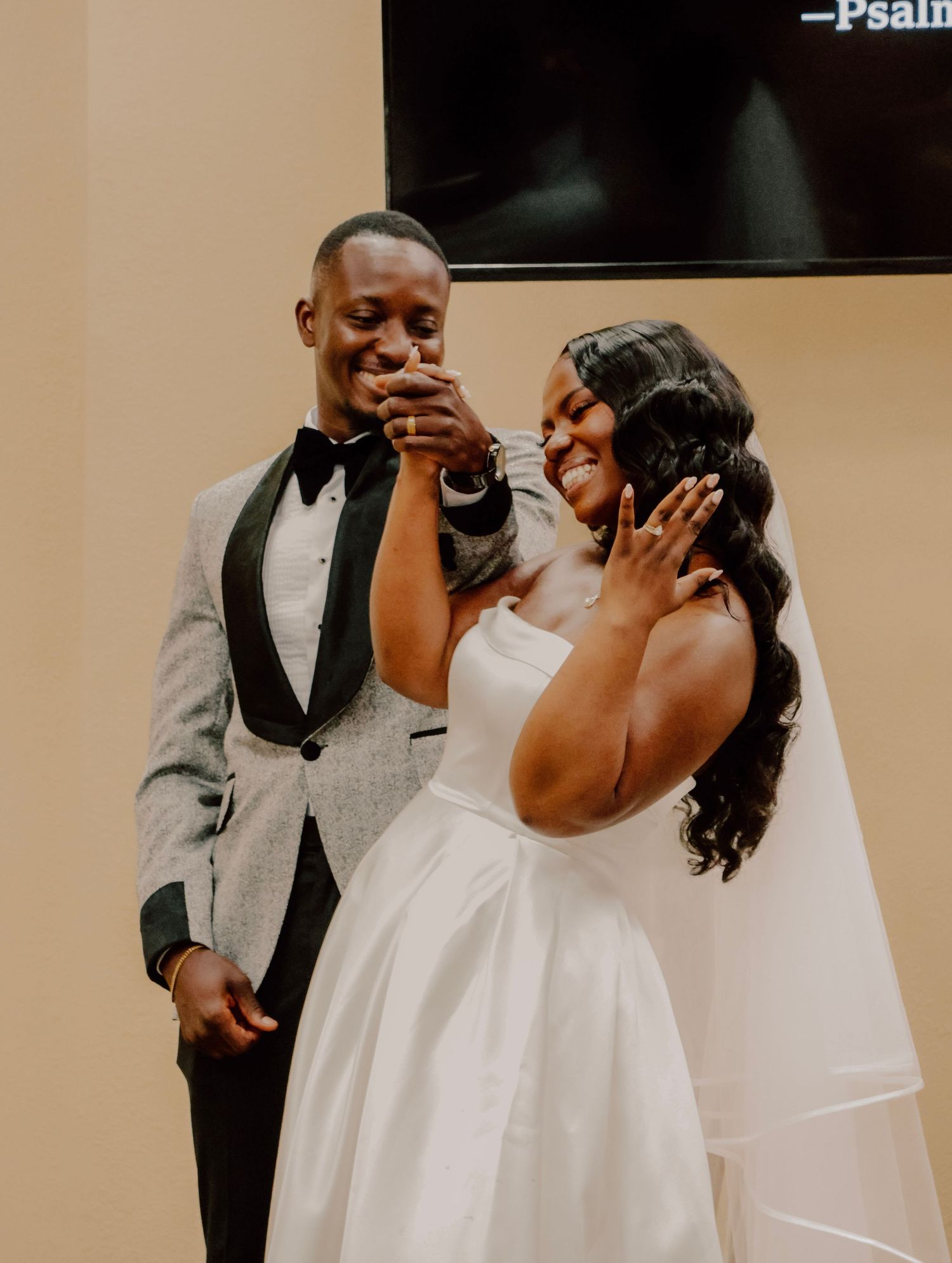 A couple celebrates an emotional moment at their wedding as the bride touches her face and groom takes a sip of champagne.