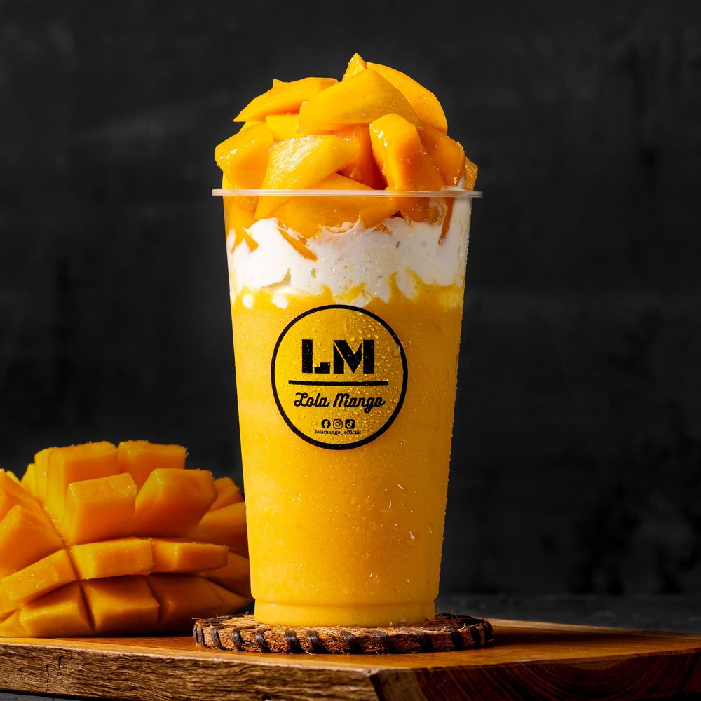Fresh mango desserts in yellow branded cups against dark background.