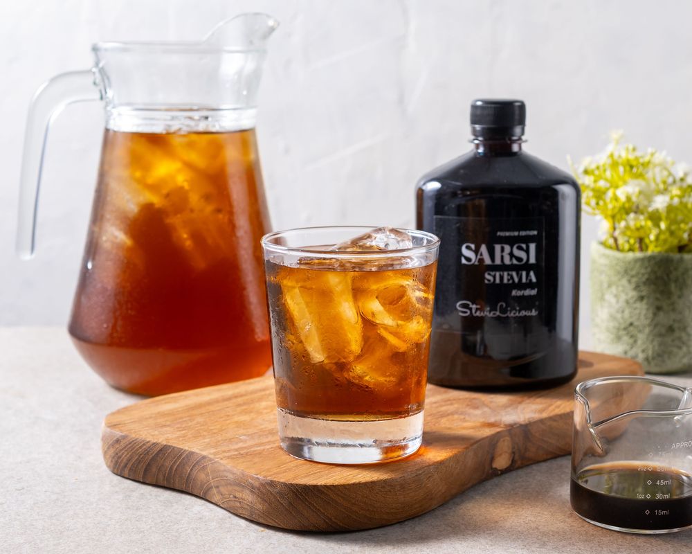 Cold brew coffee served in glass with ice on wooden board next to black bottle.