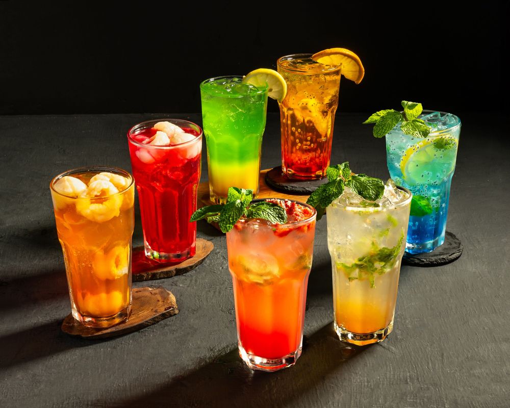 Assortment of vibrant cocktails garnished with citrus and herbs on dark background.