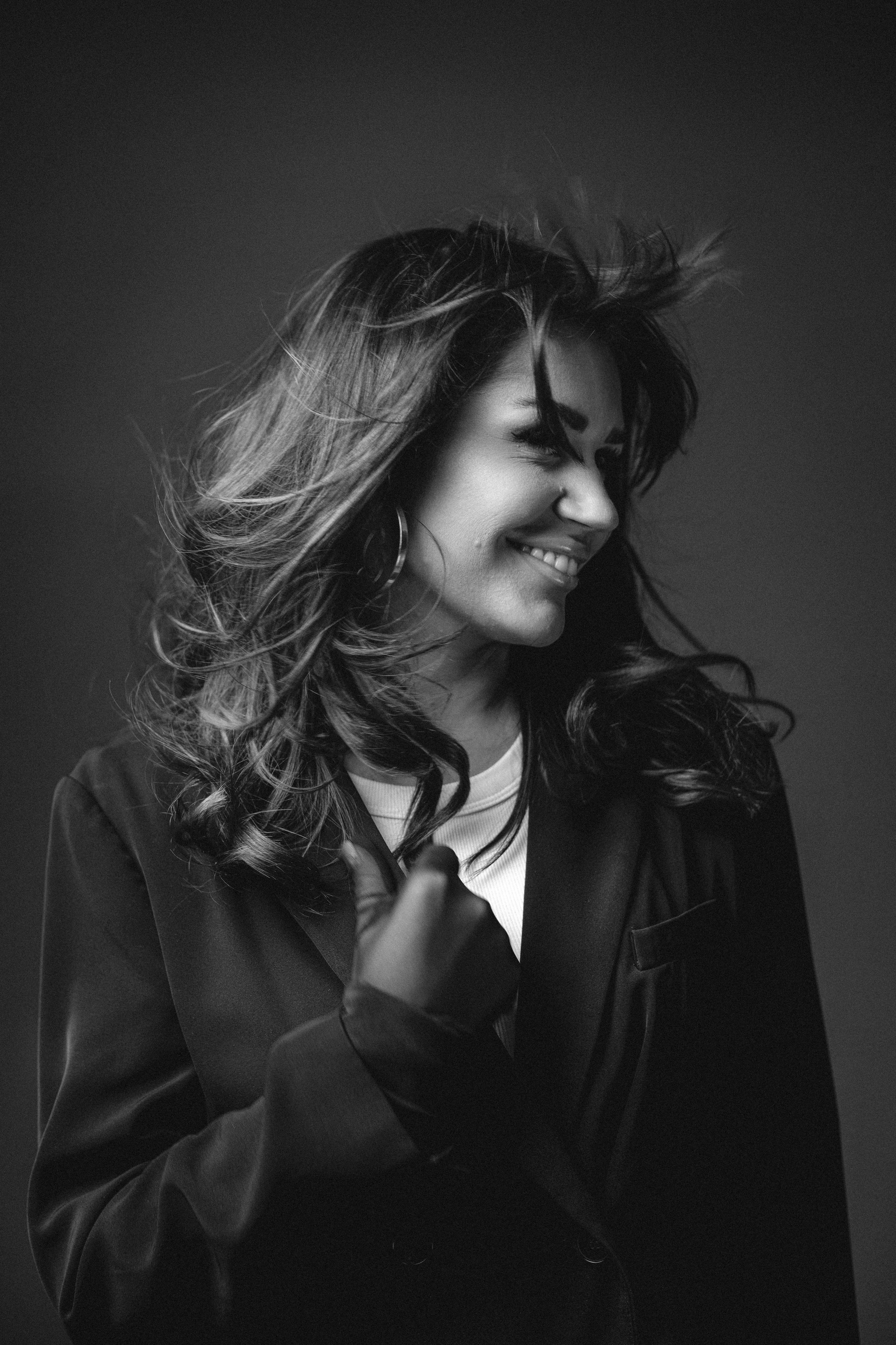 Black and white portrait photograph of a candid laughing expression with windblown hair wearing a dark jacket.