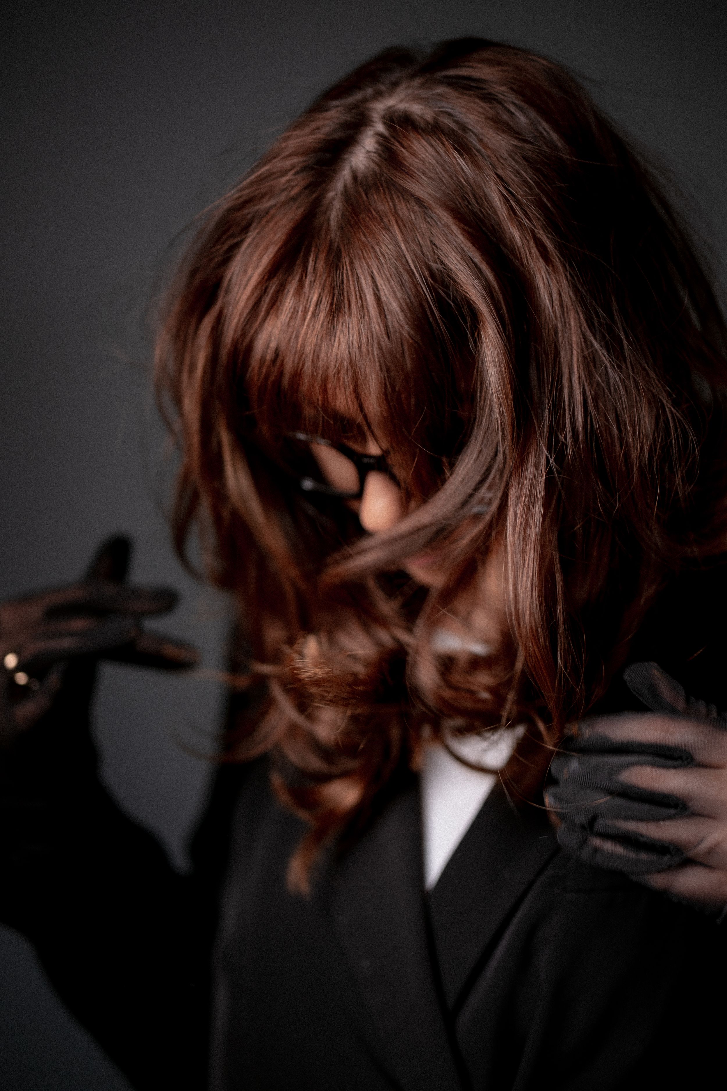 Moody portrait of figure in black with flowing auburn hair against dark background, with dramatic shadows and lighting.