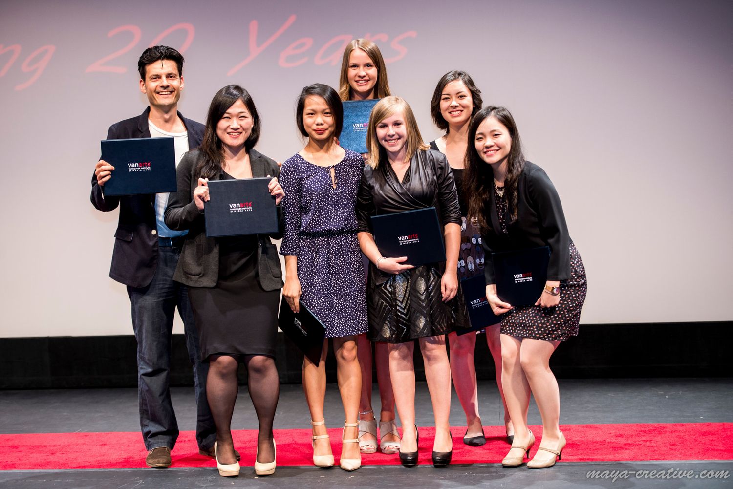 A group of professionals in business attire smiling while holding awards on a stage with a red carpet.