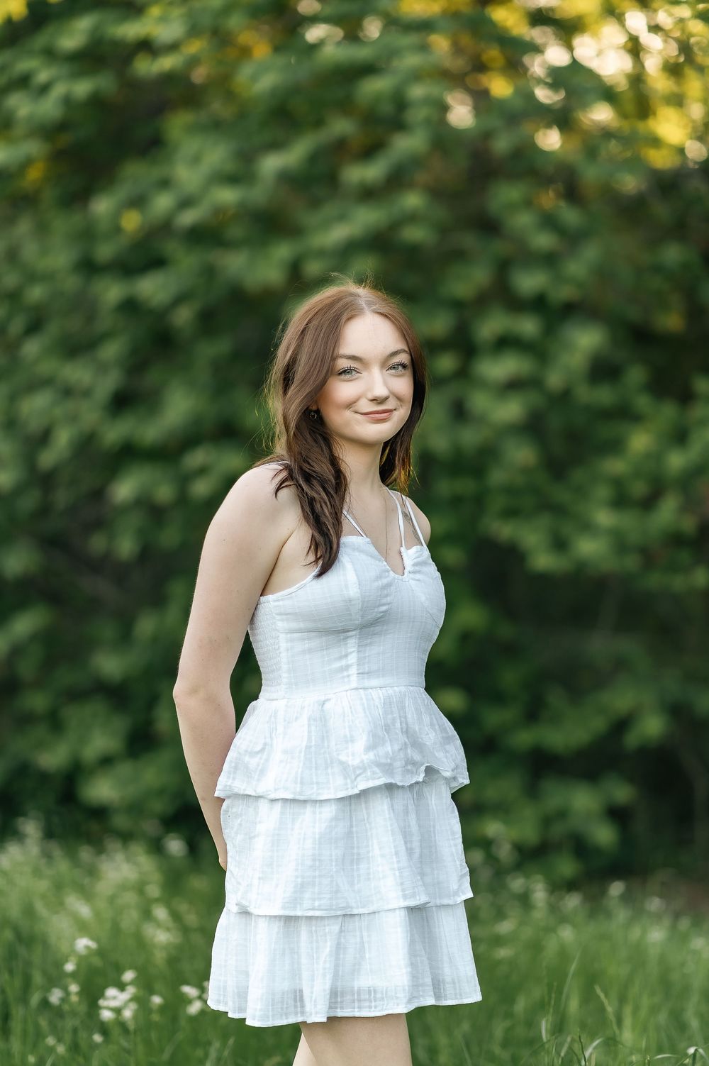 Woman in a white tiered sundress poses in a garden setting during golden hour.