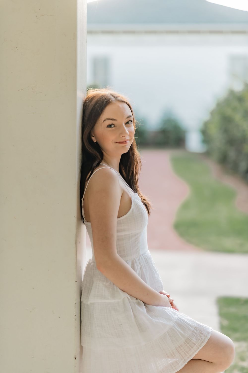 Woman in white dress leaning against column with natural outdoor backdrop.
