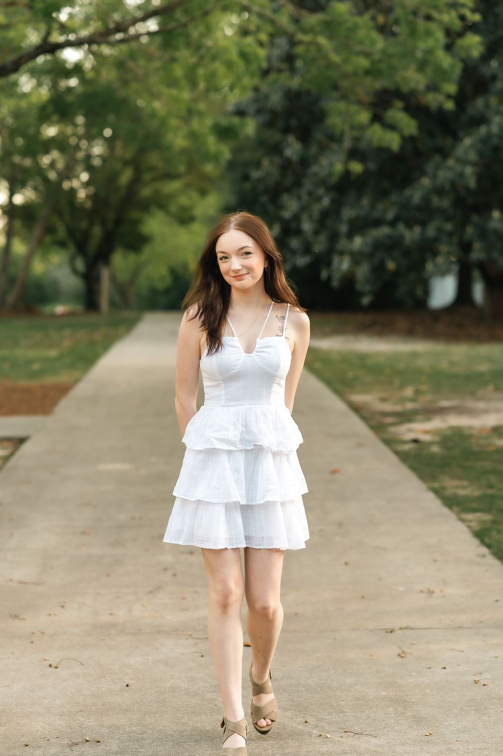 Woman walking down concrete path wearing white tiered dress and sandals.