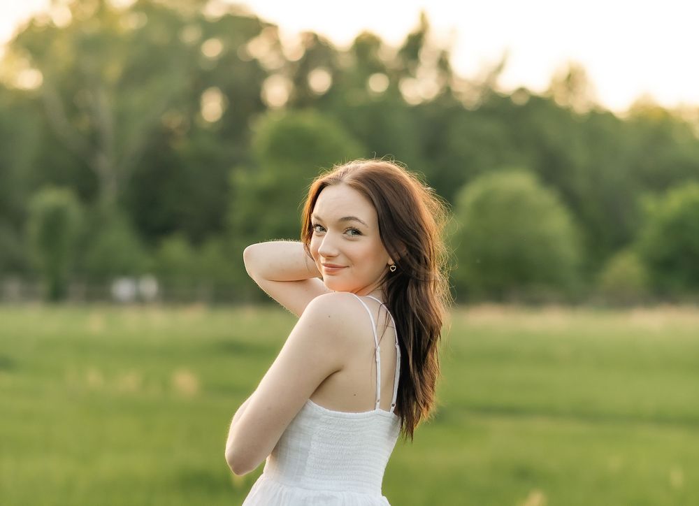Woman in white dress posing in field during golden hour with natural lighting.