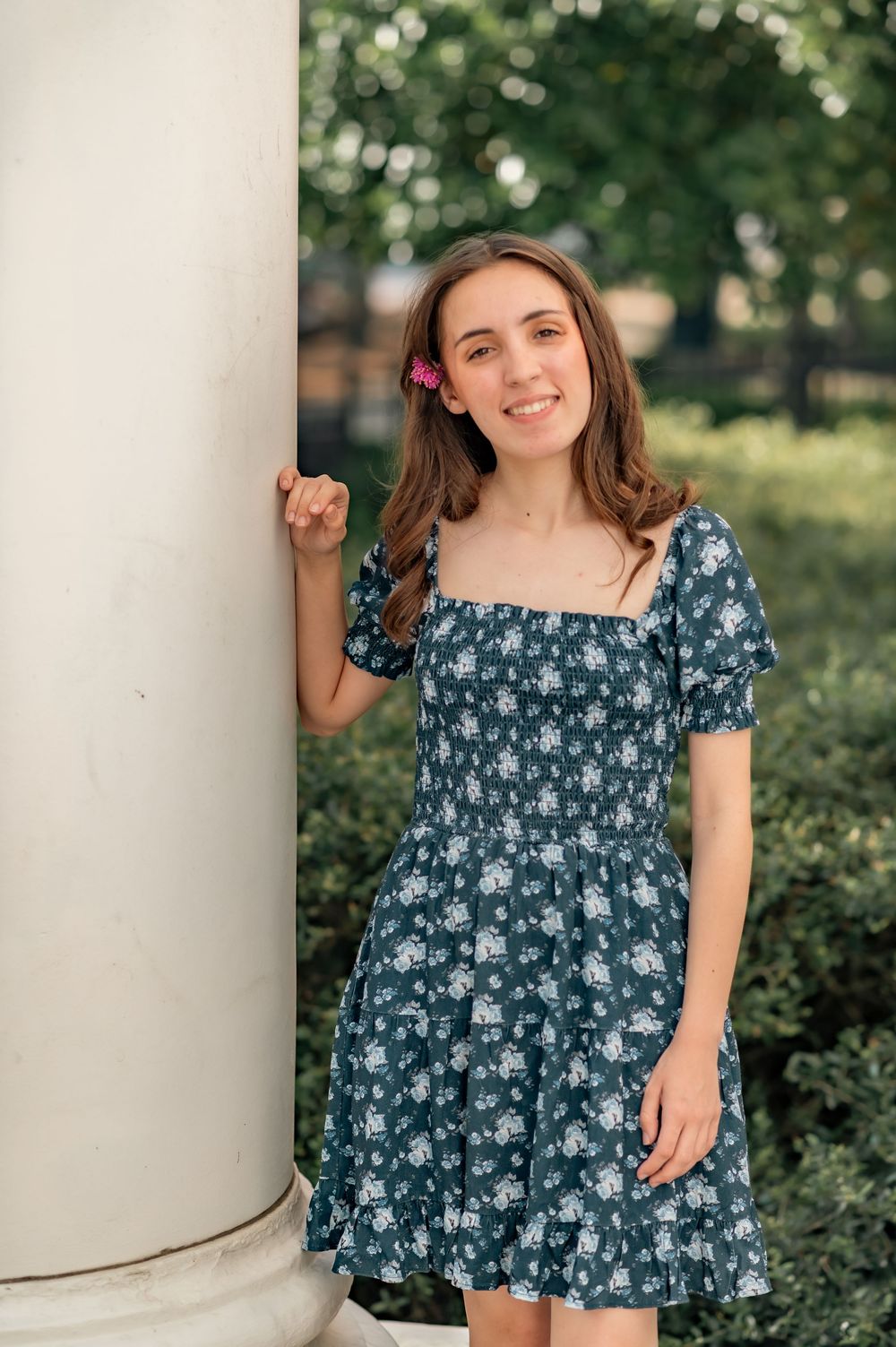 Portrait of graduate in floral navy blue dress posing against white column outdoors.
