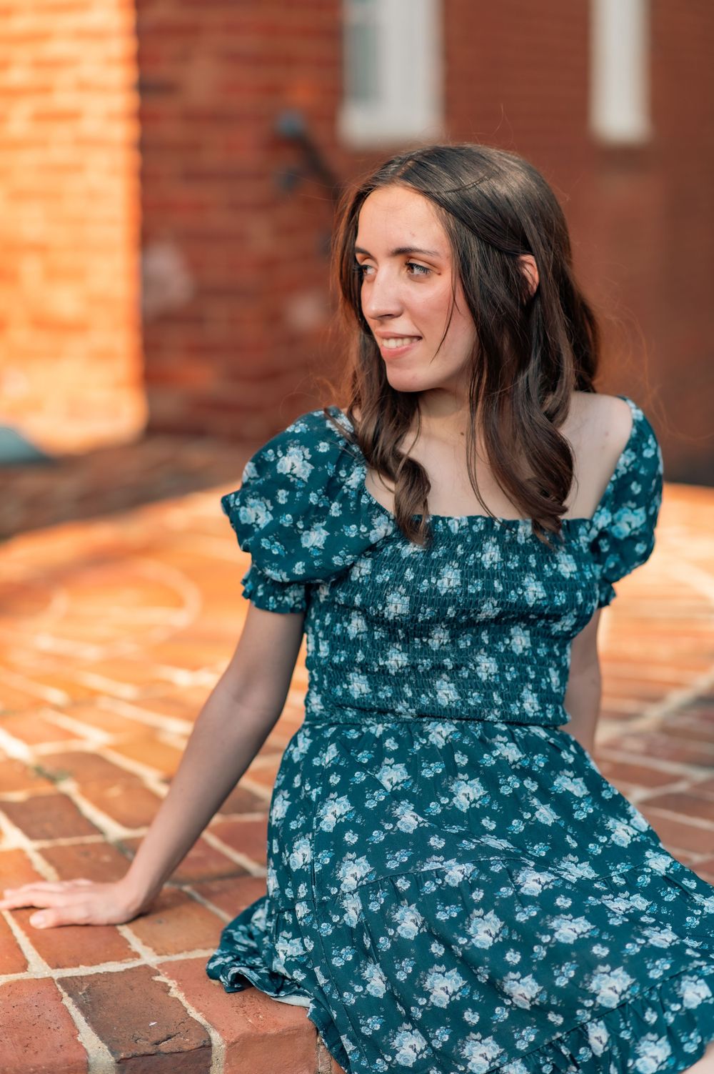 Graduate in floral dress poses on brick patio during portrait session.