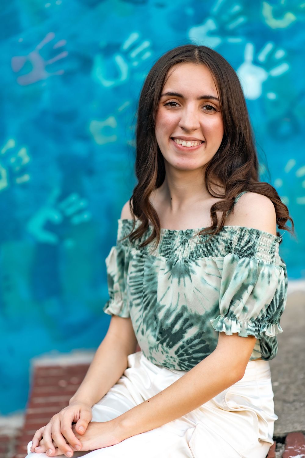 Close-up portrait of graduate against blue wall with handprint decorations.