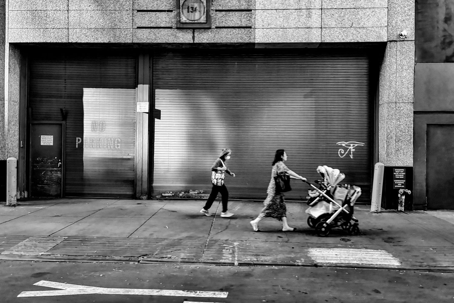 A black and white street scene showing pedestrians walking past a shuttered storefront.