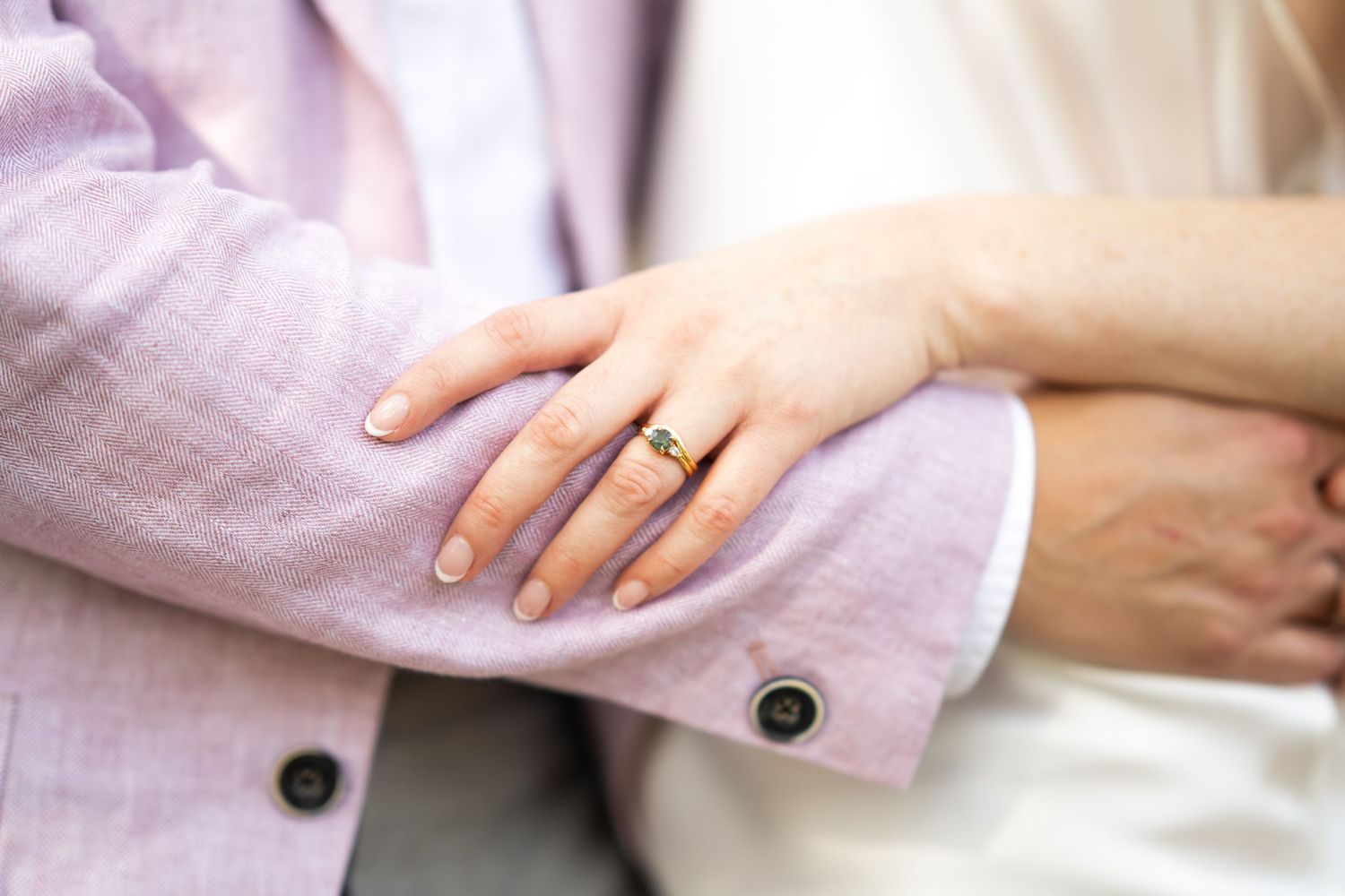 Close-up detail shot of wedding rings and hands against pink fabric.