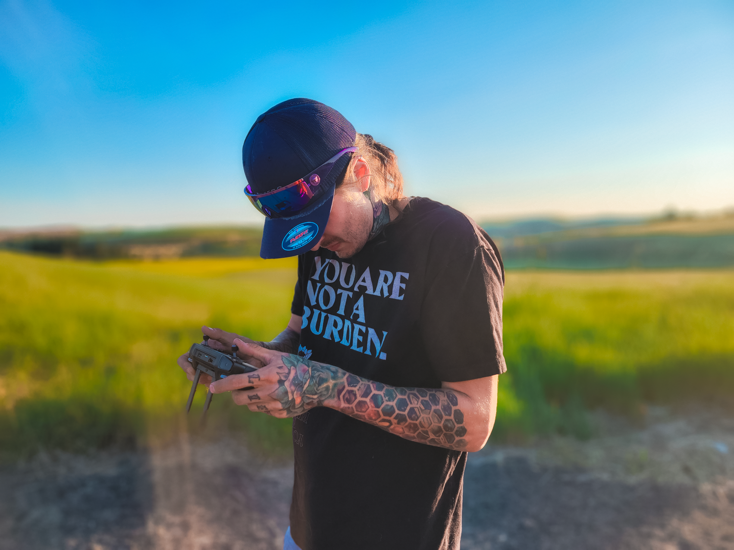 Someone checks their phone while wearing a black t-shirt and baseball cap in a sunny field.