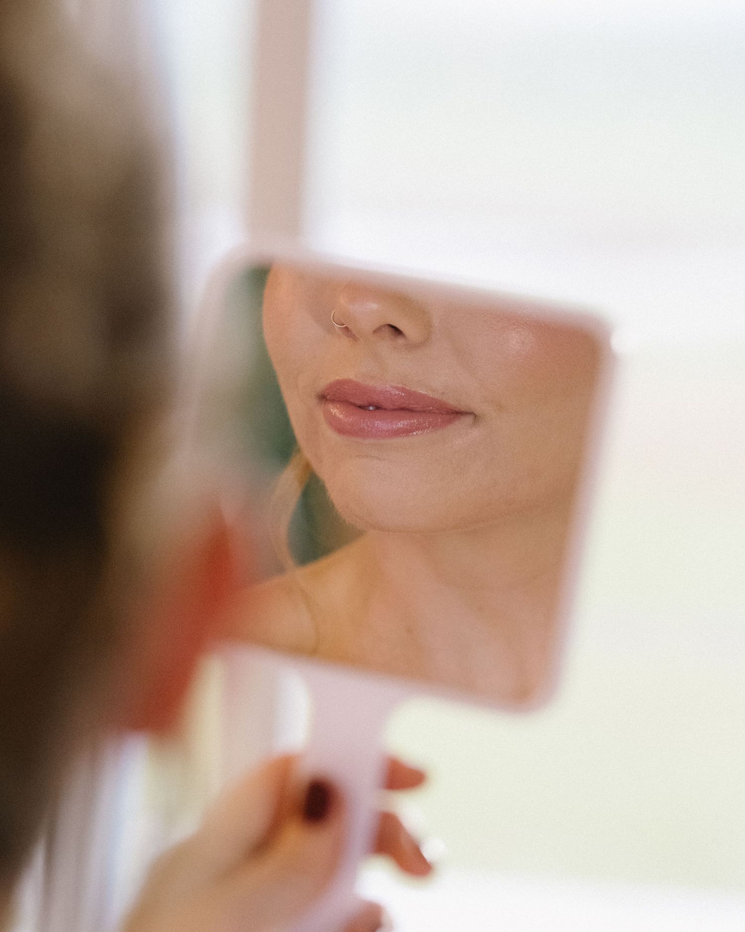 Reflection of soft smile in small mirror during wedding preparation.