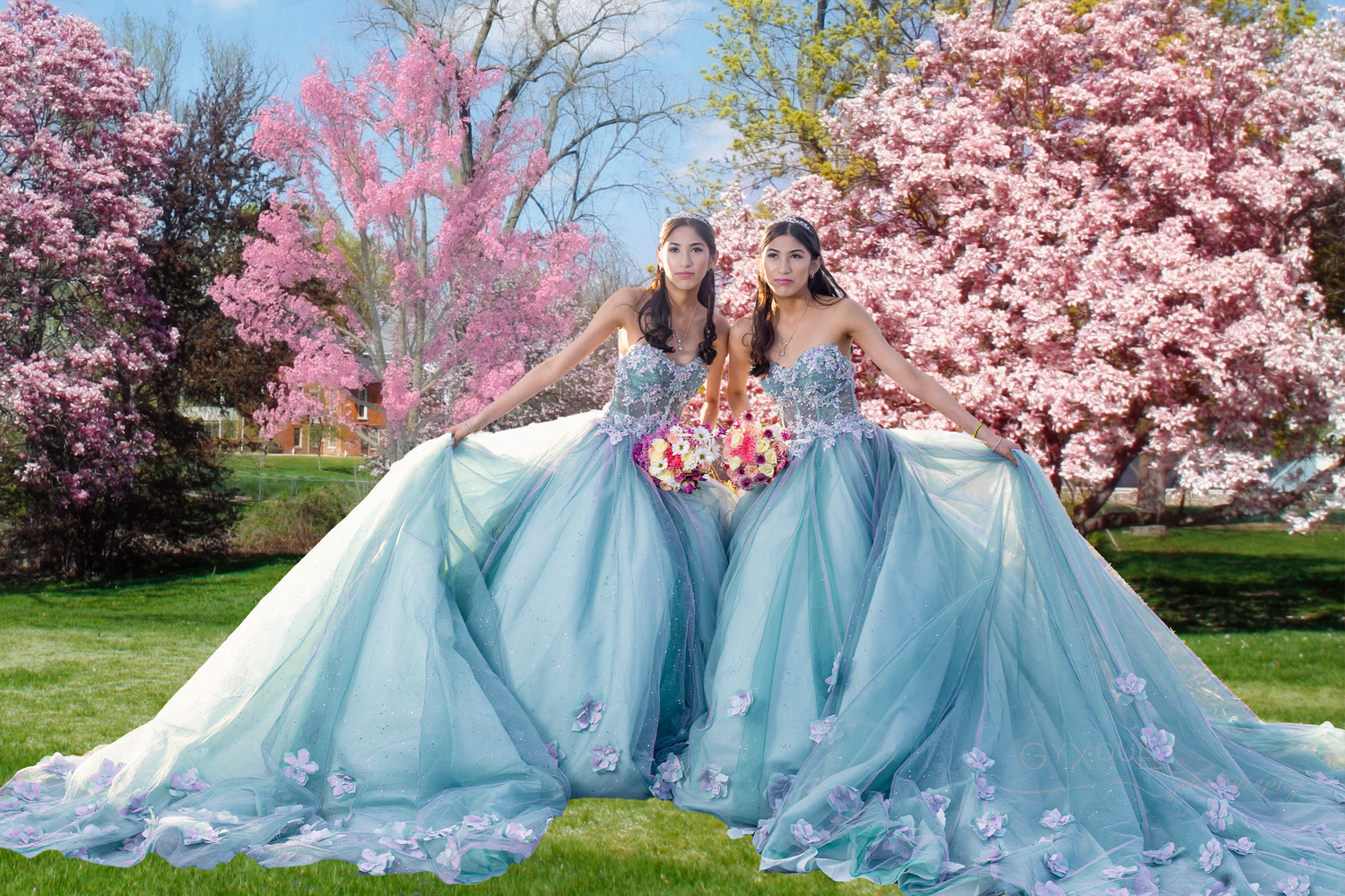 Two models in flowing ice blue gowns pose together under pink cherry blossoms.