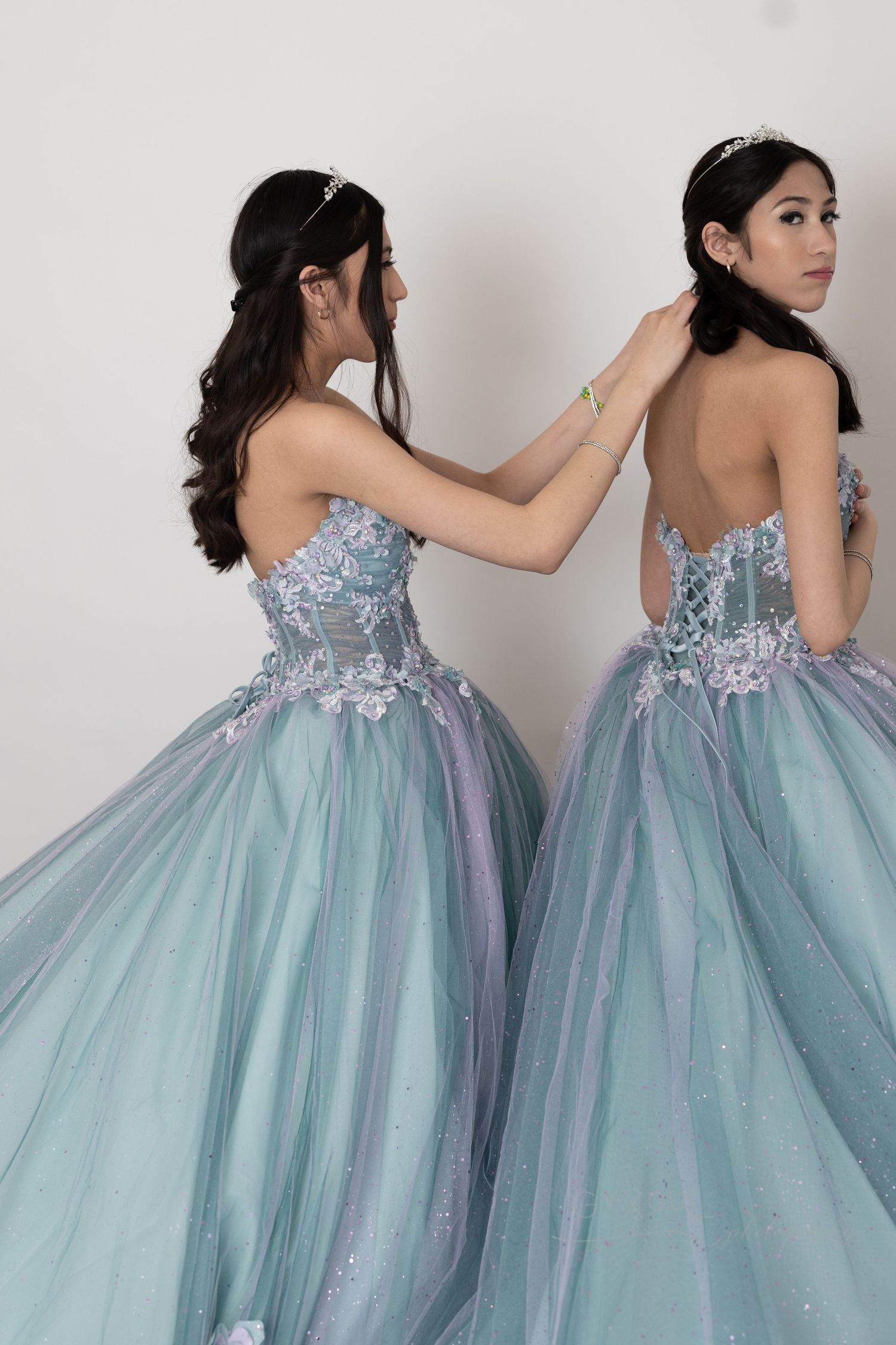 Two models in matching pastel blue tulle ball gowns with sequined bodices against white background.
