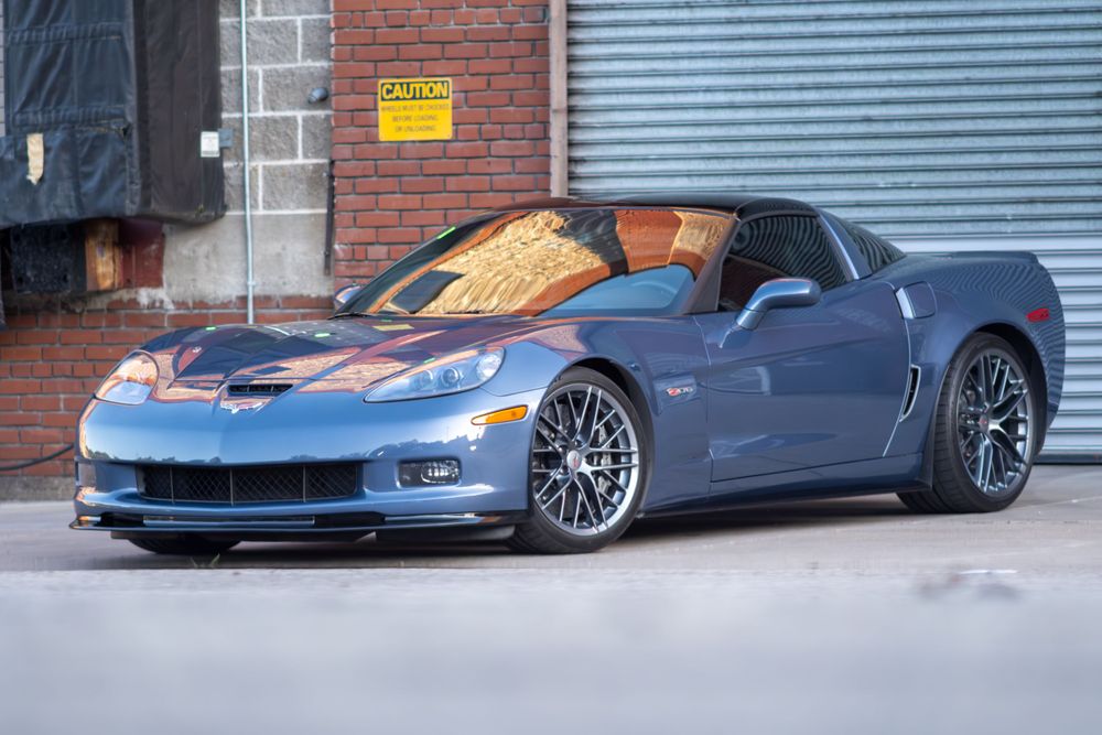 A metallic blue Chevrolet Corvette ZR1 sports car with chrome wheels parked against an industrial brick building.
