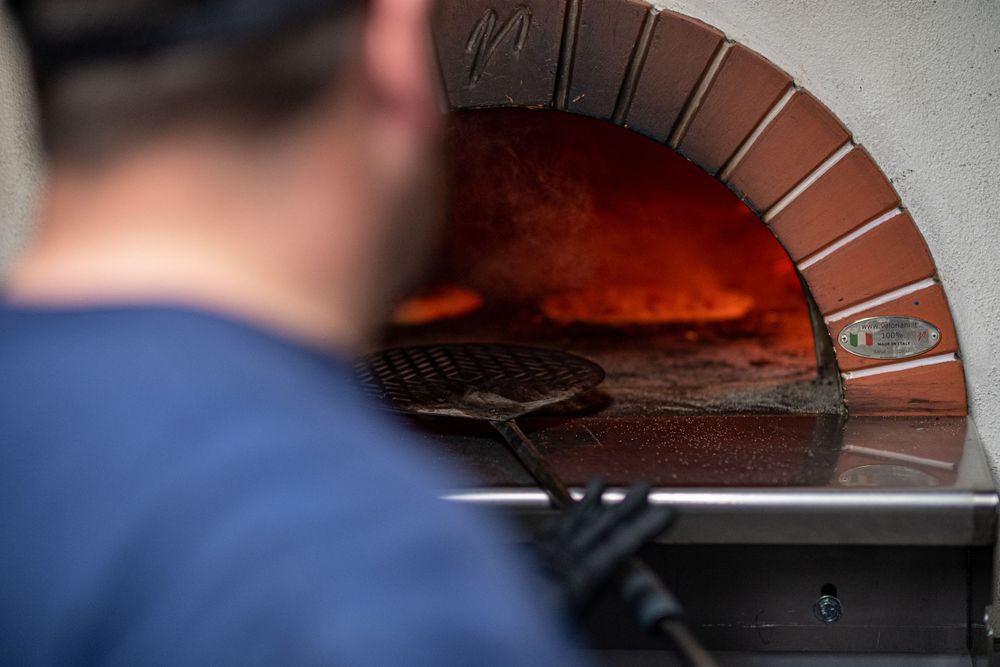 man putting pizza in brick oven