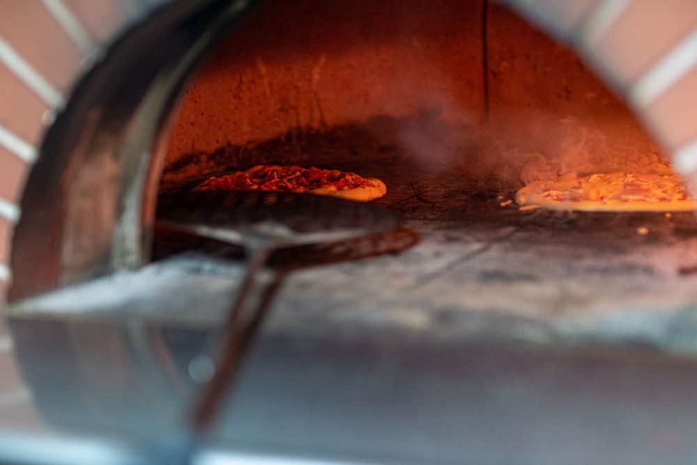Hot flames inside a brick pizza oven with rustic wood-fired cooking surface visible.