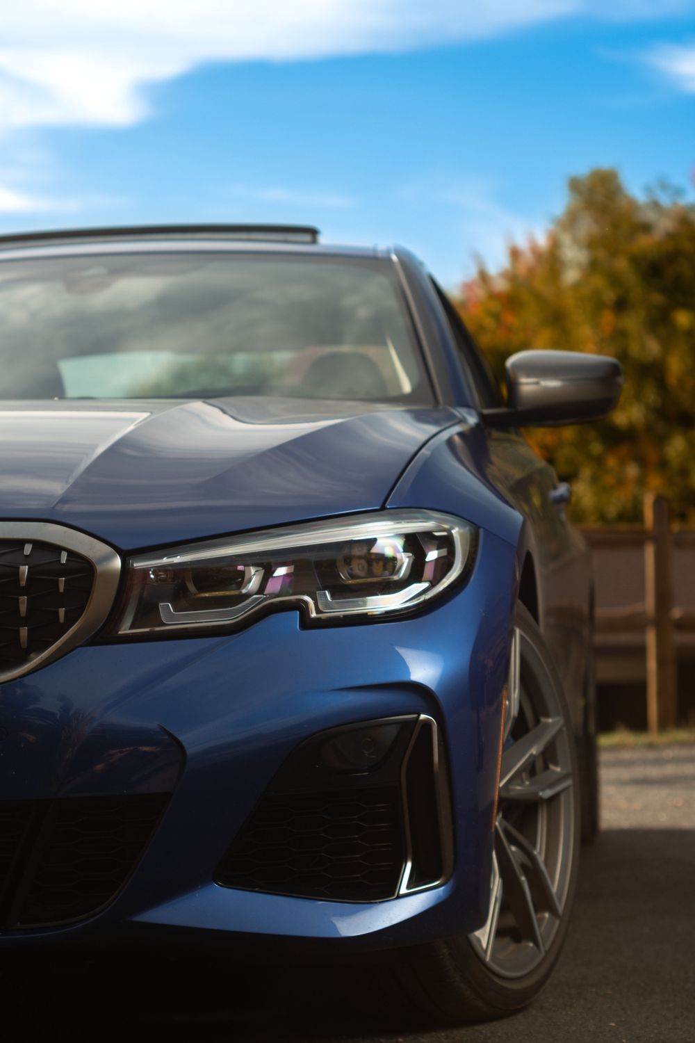 Close-up view of a blue BMW 3-series front end showing modern LED headlight design and signature kidney grille.