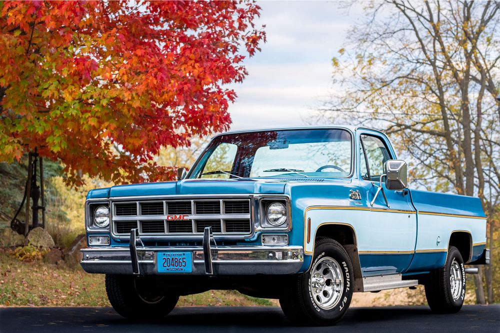 A classic blue and white Chevrolet pickup truck parked under vibrant red fall foliage on an autumn day.