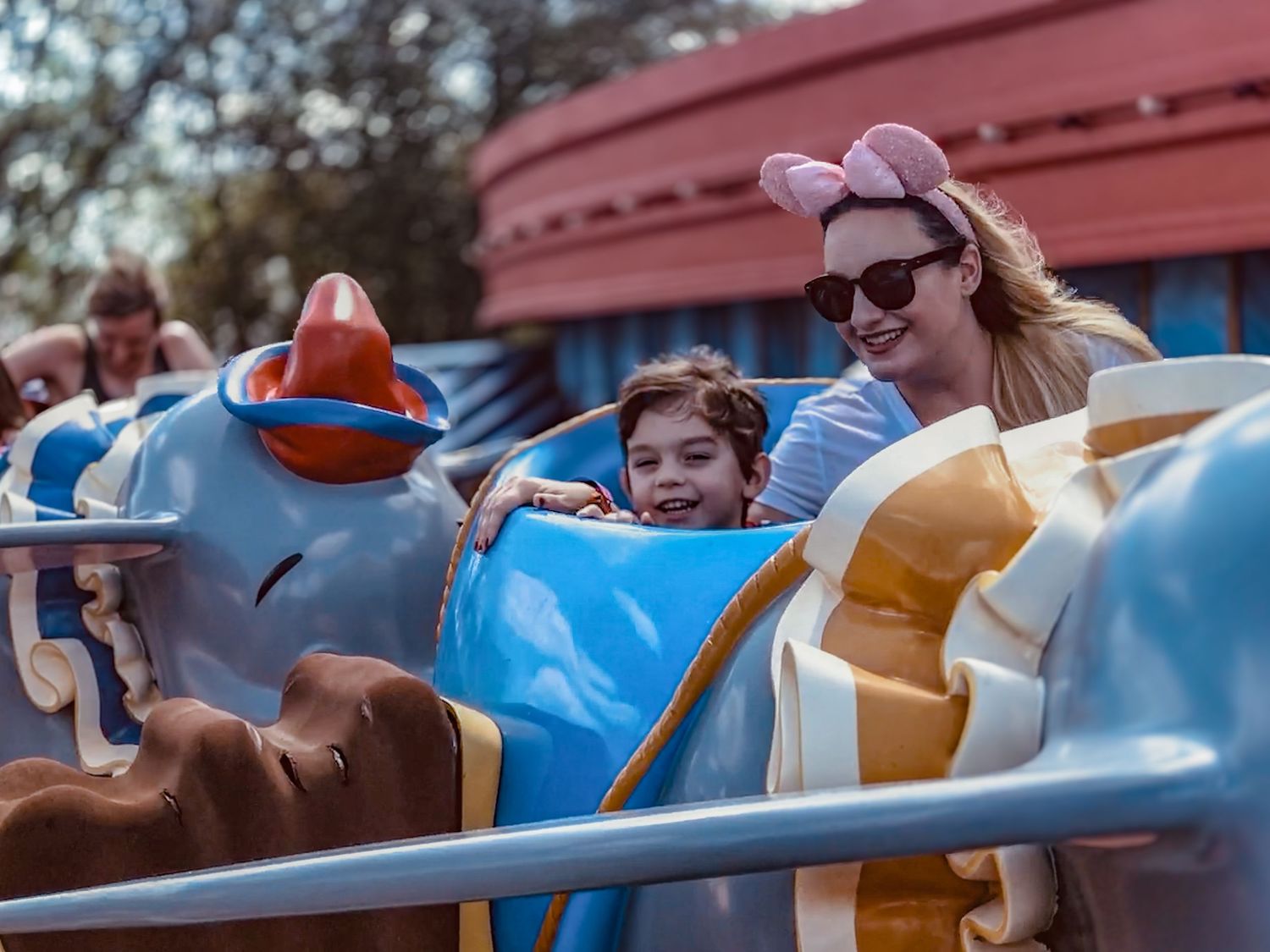 Riders enjoying a whimsical blue elephant-themed amusement park ride at a theme park.