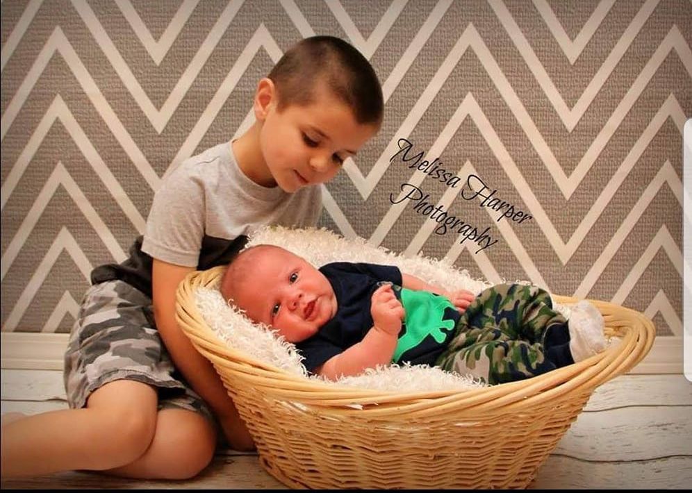 Two children sitting with a basket against a chevron patterned wall.