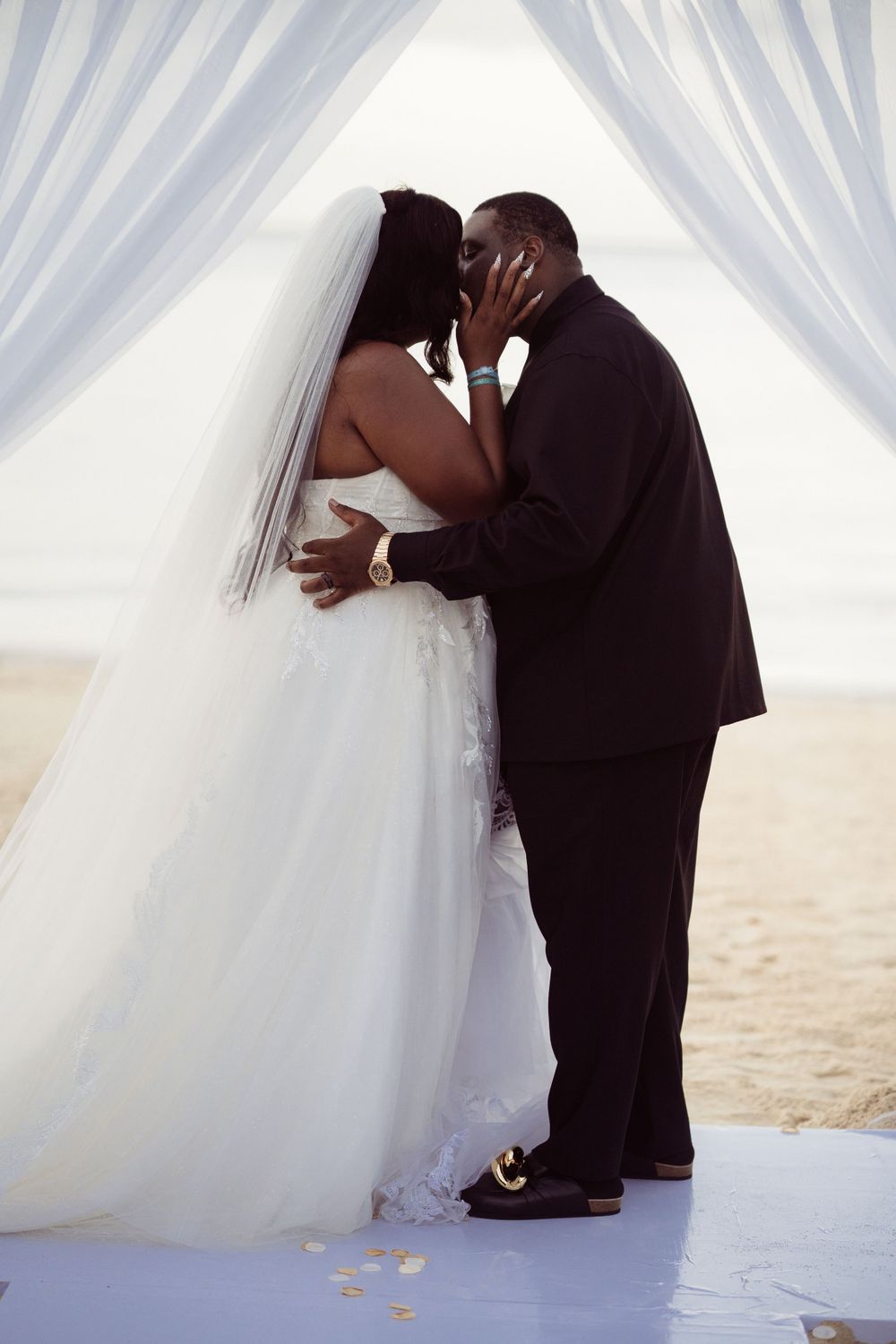A romantic beach wedding moment with a couple sharing a tender embrace under white flowing curtains.